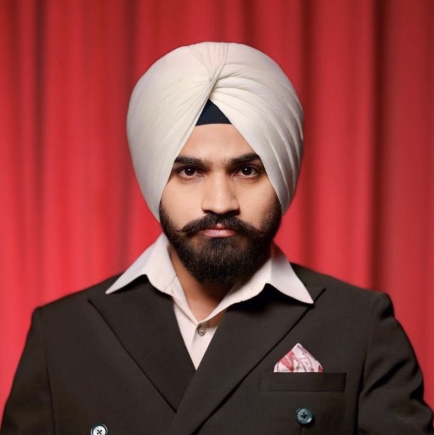 Sandeep Bhaga in a white turban and dark double-breasted suit, standing before a red curtain